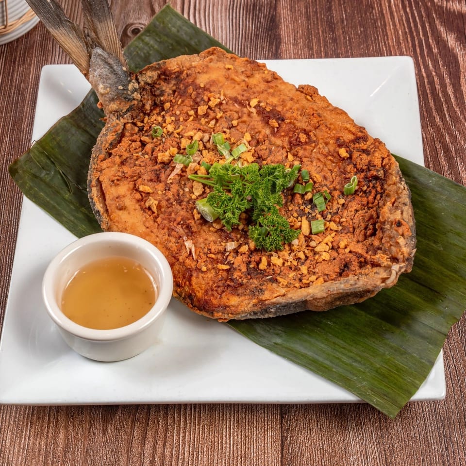 Crispy fried milkfish, or Daing na Bangus, on a banana leaf with a side of dipping sauce.