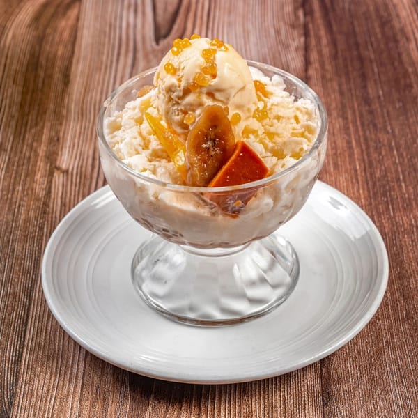Filipino Halo-Halo dessert in a glass bowl with ice cream, fruit, and boba on a wooden table.