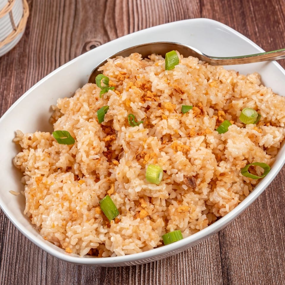 A white bowl of Filipino garlic fried rice, topped with toasted garlic and green onions.