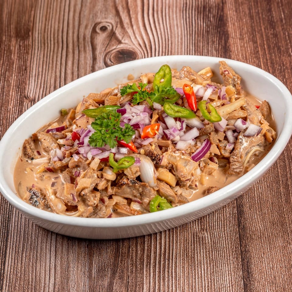 Filipino Bicol Express, a creamy pork dish with coconut milk, chili, and onions in a white bowl.