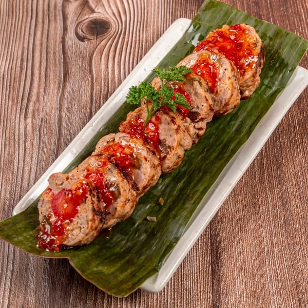 Sliced Filipino Embutido, a meatloaf dish, topped with red sauce and parsley on a banana leaf.