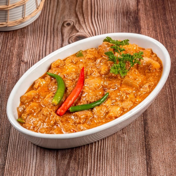 Filipino Bicol Express, a creamy pork dish with coconut milk, chilies, and parsley, in a white oval dish.